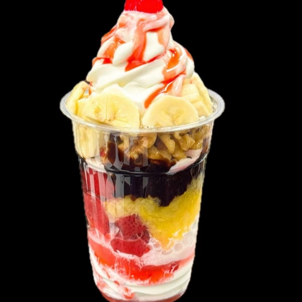 A Sabor Ice Cream banana split parfait with whipped cream, cherry, and fruit in a clear cup.